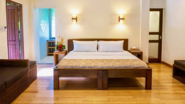 A comfortable deluxe room in an upscale boutique hotel, with a queen size bed, rattan furnishings, wooden floors, and natural light. In the Philippines. clipart