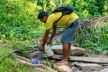 Puerto Galera, Filipinler - 24 Nisan 2021. Mindoro Adası 'ndaki yerel Mangyan kabilesinin bir üyesi, ormanın içindeki bir su borusuna kesilmiş geçici bir musluk kullanarak plastik bir sürahi dolduruyor..