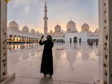 Siyah abaya giyen genç Müslüman bir kadın, Abu Dabi, BAE 'de gün batımında çok güzel bir camide selfie çekiyor..