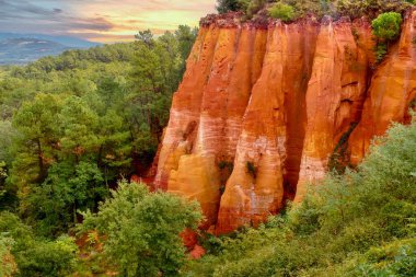 In Roussillon, France, a dramatic cliff of variegated red, orange and yellow ochre pigments in the forested area on the edge of the village, in the Luberon region of Provence. clipart