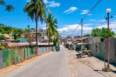 Sabang Village, Puerto Galera, Philippines - May 4, 2021: A narrow road lined with corrugated metal sheeting and simple buildings on the outskirts of a popular dive resort town on Mindoro Island. clipart