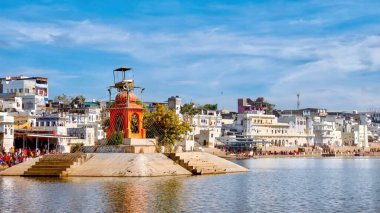 An orange monument on an artificial island in Pushkar Lake, a site sacred to Hindu pilgrims who visit the ghats to bathe in its holy waters, in Rajasthan, India. clipart