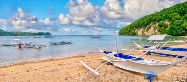 Filipinler, Puerto Galera 'da kumlu bir sahil ve körfezin panoramik manzarası. Sahilde iki geleneksel ahşap iskele teknesi ve arka planda sudaki diğerleri..