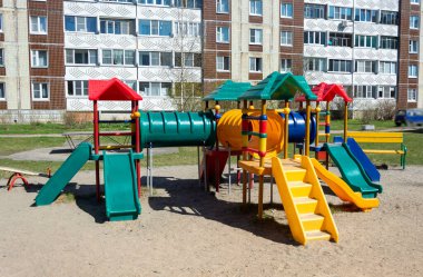 Yüksek binaların bahçesindeki oyun bahçesinde kaydırak ve merdivenlerle renkli plastik çocuk kasabası