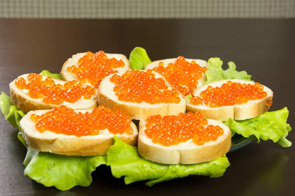 Kırmızı havyarlı lezzetli sandviç, tereyağı ve tabakta taze marul yaprakları.