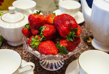 Masadaki kristal vazoda taze çilekler beyaz çay takımının arasında, tatlı olarak taze çilekler..