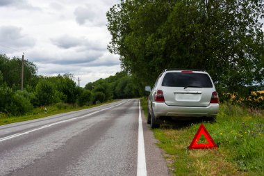 Kırsal alandaki bir arızadan sonra tamir için bekleyen bir araba, yol kenarında bozuk bir araba, acil durum dur işareti.