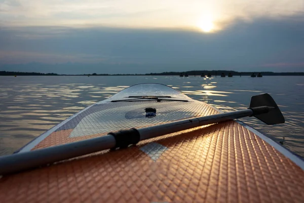 SUP board, Paddle board with a paddle in the sunset light on the background of water close-up. SUP boarding equipment. Water sports in the open air. Surfers ' lifestyle