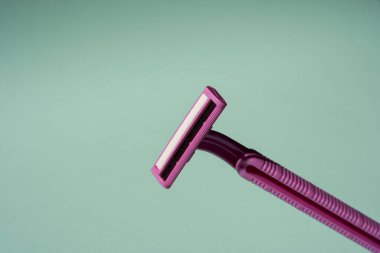 Tek kullanımlık tıraş bıçağı, turkuaz arka planda tek kullanımlık jiletin yaratıcı bir bileşimi, minimalist bir kavram.