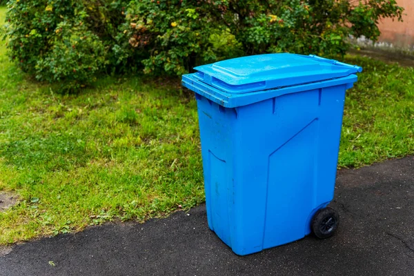Konut binasının avlusundaki plastik mavi çöp konteynırı..