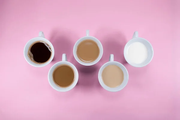 Kahve ve süt fincanları ile küçük pembe arkaplan kompozisyonu.