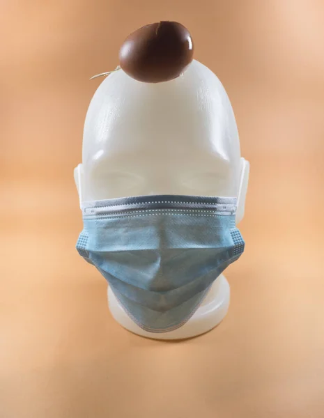 Soyut modern kompozisyon, maskeli insan yüzü, kafaya düşen paskalya yumurtası. Mavi sırtlı, maske takan ve düşen bir Paskalya yumurtası takan bir insanın asgari kompozisyonu. Mahvolmuş tatil kavramı.
