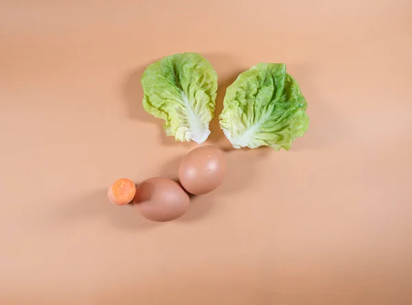 以橙色为背景的复活节彩蛋和蔬菜的最小抽象的现代构图 代表复活节兔子 莴苣叶子代表兔子耳朵 — 图库照片