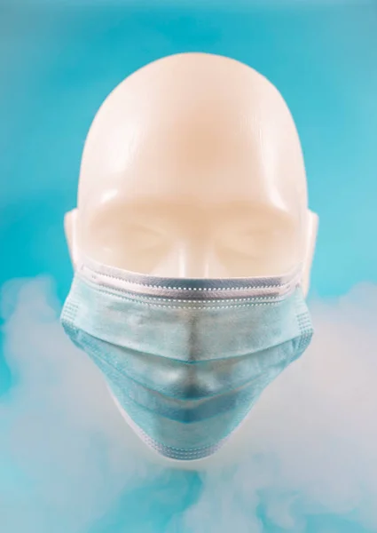 Minimal abstract composition background of a human face wearing a mask, covered in smoke, on a soft blue background. Pandemic concept.