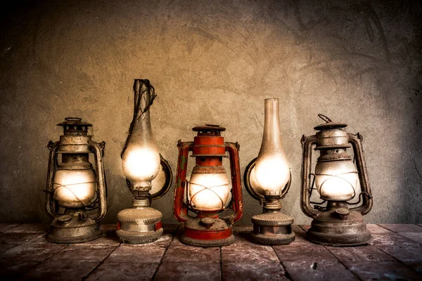 Old, antique oil lamps on tiles with concrete wall background. Vintage house appliances.