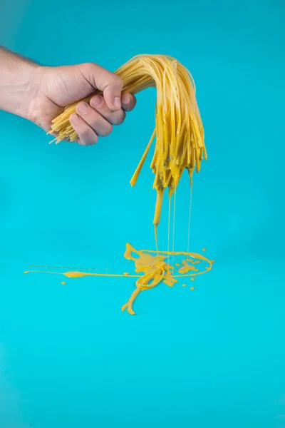 Yarı pişmiş, sarı boyalı bir spagetti. Turkuaz mavi arka plan. Asgari soyut gıda fikri. Boyama konsepti. Kopyalama alanı ile.