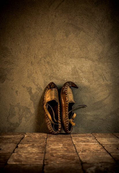 Old rustic  footwear made of leather on antique tiles and concrete wall background. Vintage clothes idea. Old national shoes. 