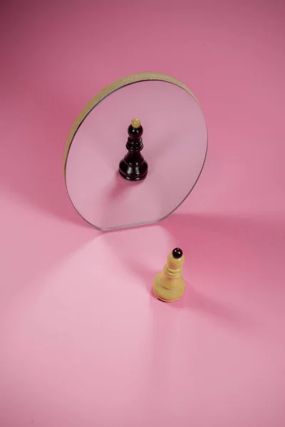 Chess piece white bishop with black reflection in a mirror. On trendy pastel pink background. Optical illusion. Minimal abstract different personalities idea.