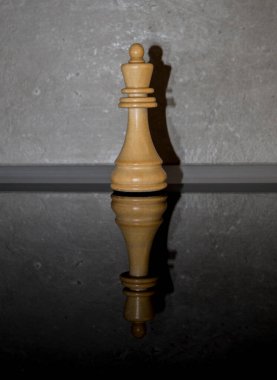 Tahta beyaz satranç taşı, koyu ayna camının üzerinde beton arka planı olan bir kral. Oyunlar, spor ve eğlence fikri. Asgari soyut zeka ve strateji kavramı.