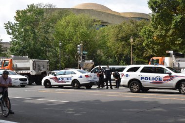 Washington, DC, ABD - 18 Eylül 2021: Polis memuru, polis arabaları ve DC belediye kamyonları, arka planda Smithsonian Yerli Amerikan Müzesi ile J6 protestosu için Adalet Karşısındaki Üçüncü Cadde 'de güvenlik bariyeri görevi görüyor