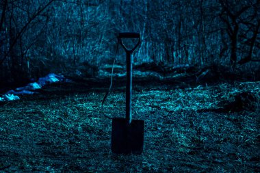 Gece ormanının bulanık arka planında gizemli ve korkutucu bir kürek. Etrafta kimse yok.
