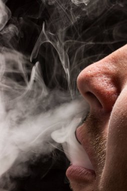 Gri sigara dumanı, arka planda sigara içen birinin açık ağzından çıkar. Zevk ve rahatlama kavramı.