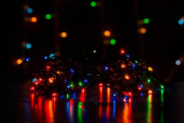 Yüzeyden yansıyan siyah bir telle parlak renkli çelenkler Noel ve Yeni Yıl şenlik ışıkları kavramının bulanık arka planında