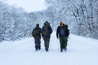 Erkekler sırtlarında uzun ağaçlar, sırt çantaları, kış patikaları boyunca yürürler.