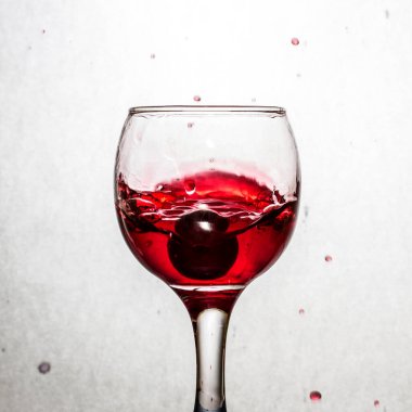 Düşen üzümlerden parlak bir şekilde kırmızı şarap sıçratmak. Popüler bir alkolik içeceği olan gri bir arka plan konsepti.