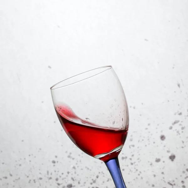灰色の抽象的な背景に斑のある色の脚を持つ傾いたガラスの明るいワイン — ストック写真
