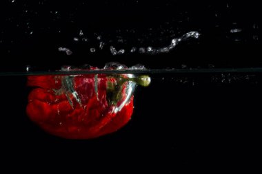 Kırmızı biber suya koyu bir arka planda düştü ve yiyecek ve sebze kavramının yüzeyinde bir su sıçraması yarattı.
