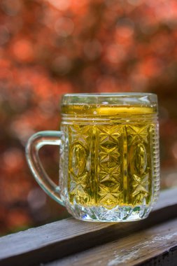 Bir bardak light bira, sonbahar portakal yaprağı konseptinin bulanık arka planında, ahşap bir pencere eşiğinde duruyor.