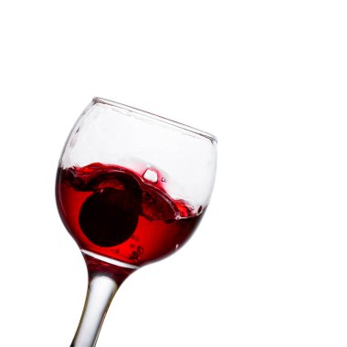 Beyaz bir zemin üzerine eğilmiş kırmızı şarap bardağı parlak bir sıçrama ve düşmüş üzümler