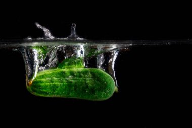 Sivilceli yeşil bir salatalıktan gelen koyu bir arka planda parlak bir su sıçraması yemek ve sebze kavramı.