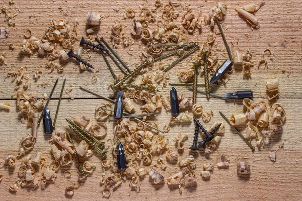 Tahta bir işyerindeki tornavida için çivi ve vidalar etrafa saçılmış. Endüstri ve ahşap işçiliği kavramı ince çiplerle kaplıydı.