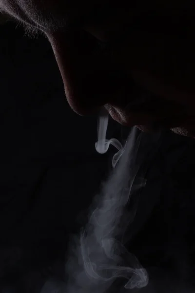 从一个抽烟的人的嘴巴和鼻子里冒出的淡淡的灰蒸汽的美丽图案接近一个黑暗的背景的概念 上瘾和坏习惯 — 图库照片