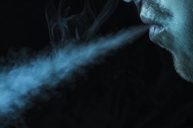 Adam sigara dumanını karanlık bir arka plan konsepti olan sigara ve kötü alışkanlıklara bırakıyor.