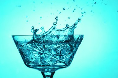 Parlak bir arka planda, eski bir bardakta, nefes kesici bir su sıçraması.