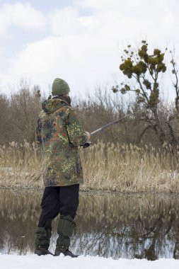 Kamuflaj yapan balıkçı mavi gökyüzünün altında nehirde balık tutuyor. İlk bahar balık tutma kavramının güzel ve parlak doğası.