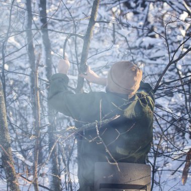 Adam kış ormanında ince bir dalı büküyor. Kamp ateşi için oduna ihtiyacı var.