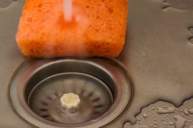 Bulaşıkları yıkamak için süngere su dökülüyor.