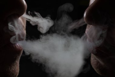 İki nefes ver. Gri sigara buharı. Arka planda sigara ve bağımlılık kavramına yakın çekim.