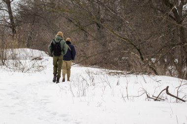 Erkekler kış ormanına doğru yol alıyorlar. Karlar içinde uzanan ve çıplak ağaçlar arasında çok güzel duruyorlar.