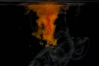 Yoğun turuncu boya, koyu bir arka planda suda çözünür. Tasarım için güzel bir soyutlama.