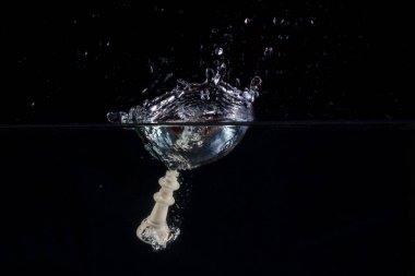 Satranç kralı, suyun yüzeyinde güzel bir sıçrama oluşturdu. Karanlık arka planda uçan sıçramalarla.