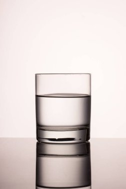 Gri arka planda cam ve şeffaf su bardağı bir masaya yansıyor.
