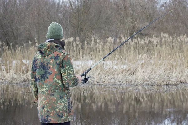 川を背景に手回しで回転するカモフラージュの漁師と釣りの葦の概念 — ストック写真