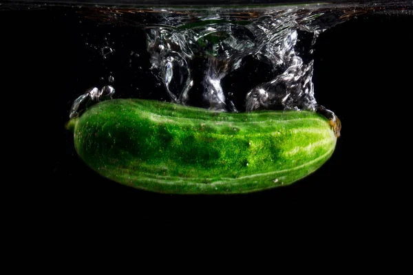 Suyun altında sivilceli parlak yeşil salatalık. Koyu bir zemin üzerinde su sıçraması. Sebze ve yemek kavramı.