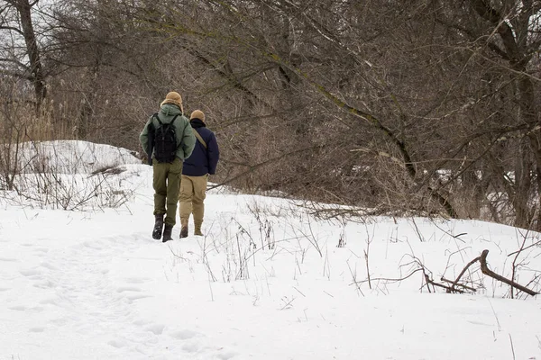 Erkekler kış ormanına doğru yol alıyorlar. Karlar içinde uzanan ve çıplak ağaçlar arasında çok güzel duruyorlar.