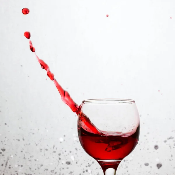 鮮やかな赤のガラスから美しいワインのスプラッシュが灰色の背景に落ちアルコールの飲料概念からスポット — ストック写真